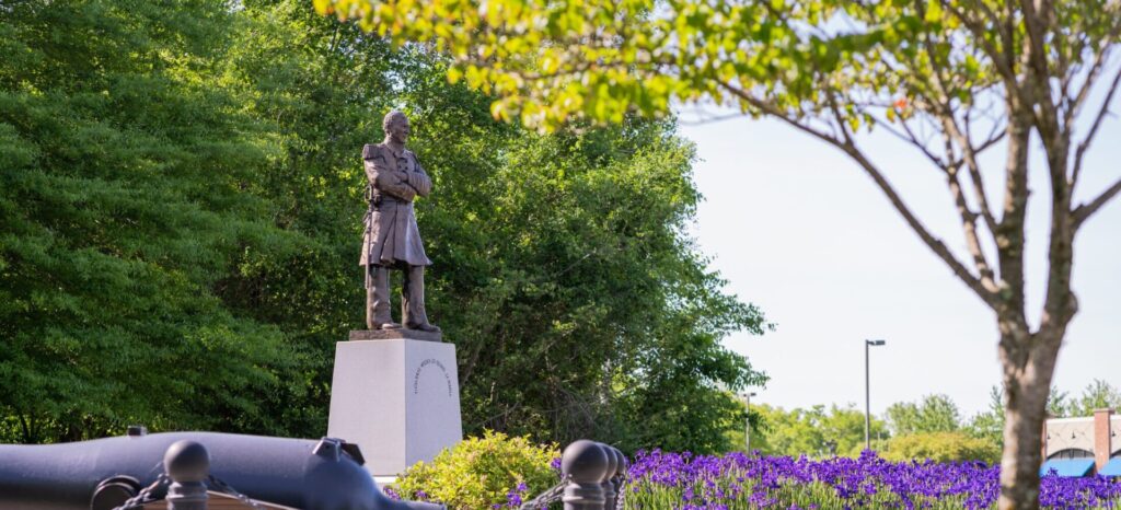 Statue of Admiral David Farragut in a landscaped park in Farragut, Tennessee, surrounded by greenery, flowers, and trees under a clear sky.