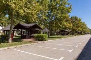 Empty parking lot in summer lined with trees and shaded picnic shelters under clear blue skies.