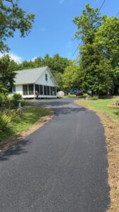 Newly paved residential driveway completed in spring, featuring smooth black asphalt curving toward a home surrounded by trees and greenery.
