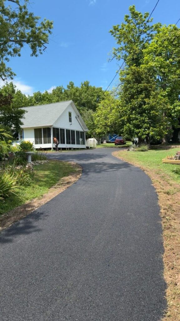 Newly paved residential driveway completed in spring, featuring smooth black asphalt curving toward a home surrounded by trees and greenery.
