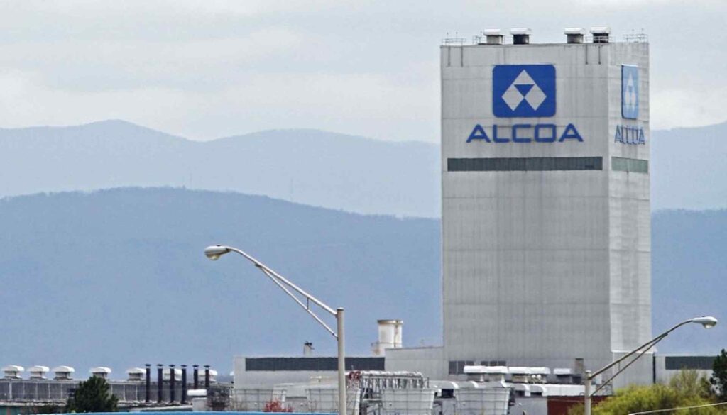Industrial facility with ALCOA tower, surrounding plant infrastructure, and mountainous landscape in the background.