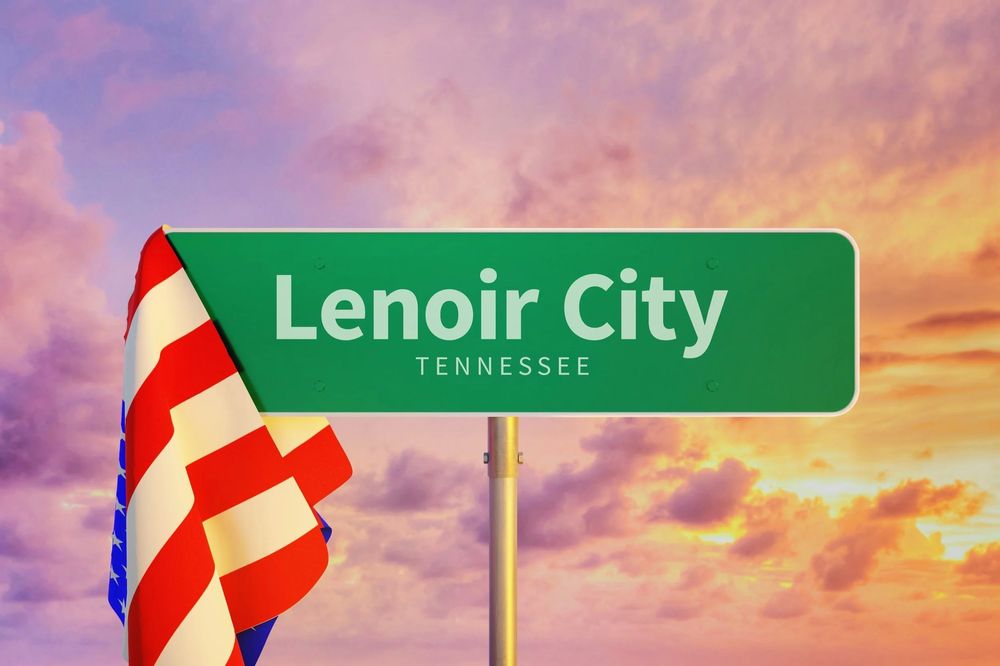 Green welcome sign for Lenoir City, Tennessee, displayed against a colorful sunset sky with a partially visible American flag in the foreground.