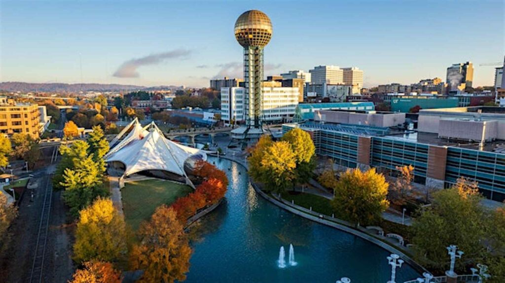 Aerial view of downtown Knoxville, Tennessee, featuring the Sunsphere, waterfront park, and surrounding buildings with fall foliage.