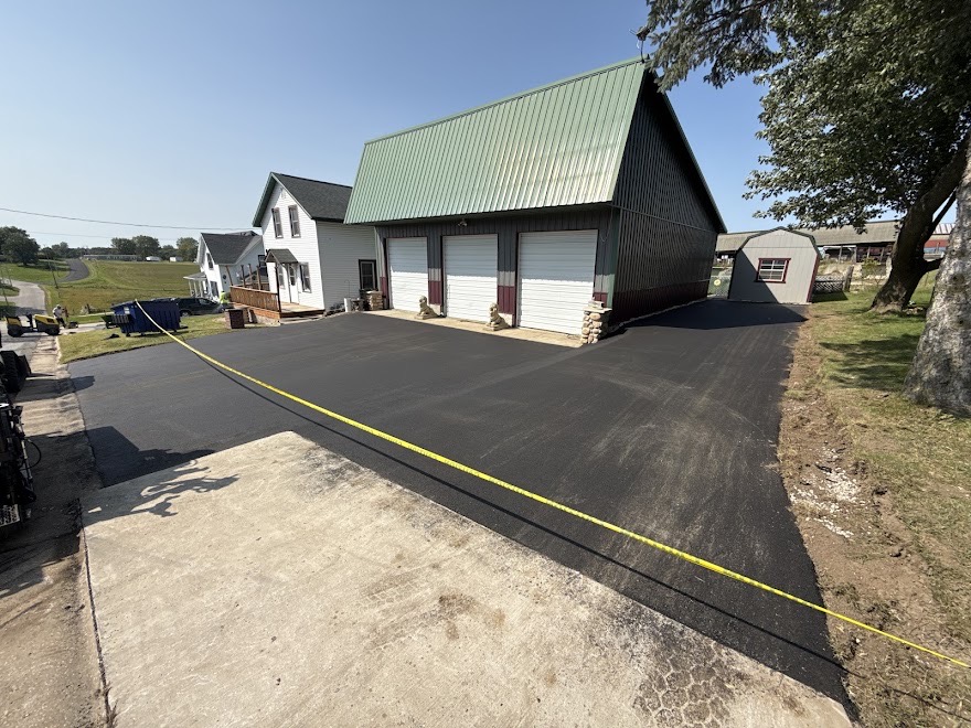 Newly paved blacktop asphalt driveway in front of a large three-car garage with a green metal roof in Halls Crossroads, TN, by Edward's Black Top Paving.