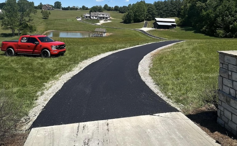 Curving blacktop asphalt driveway leading up a green hilly rural property